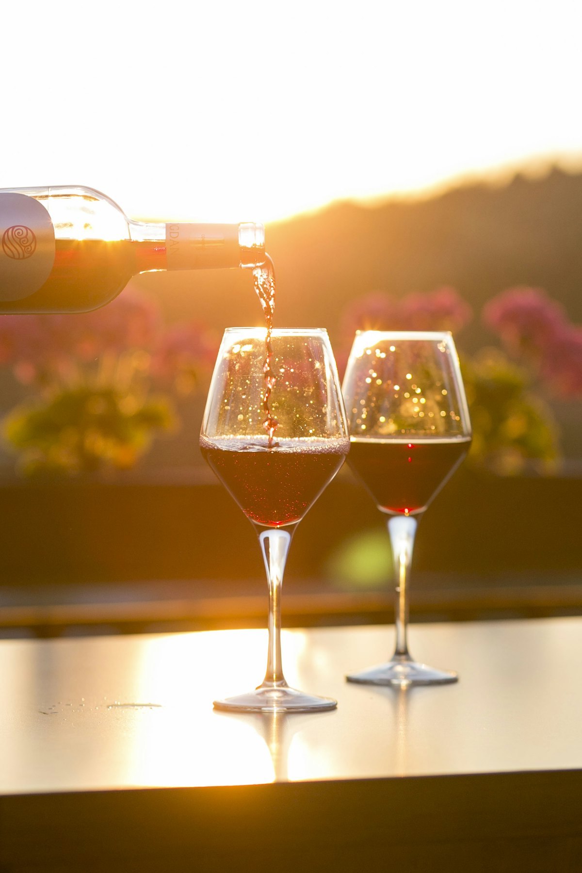 Vinho tinto a ser servido em dois copos à luz dourada do fim de tarde
